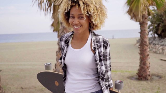 Sexy beautiful girl with blond afro haircut holding longboard on tropical beach promenade