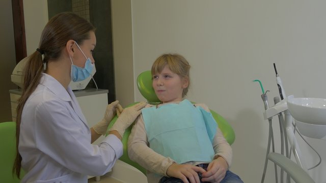 Dentist Calms a Girl Kid Nods Agrees Young Doctor is Going to Examine or Treat a Teeth of a Patient at Dental Treatment Room Visit to the Dentist