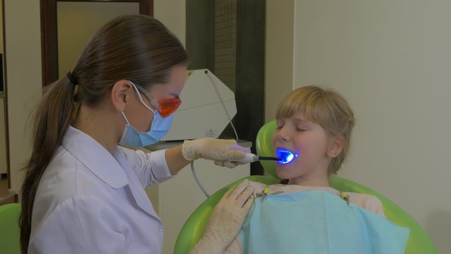 Dentist is Using a uv Lamp Patient is Smiling Doctor in Glasses and Mask is Treating a Teeth of a Patient at Dental Treatment Room Visit to the Dentist