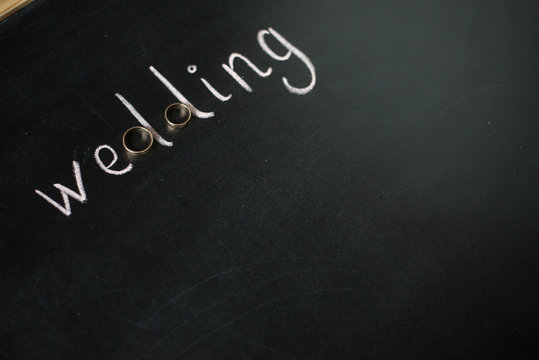 Wedding composition. Gold rings and the word "Wedding" drawn with chalk on the black board.