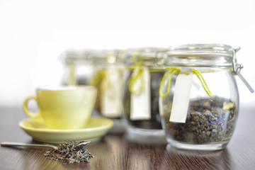 tea in spoon, glass jars and cup on wooden table with white background