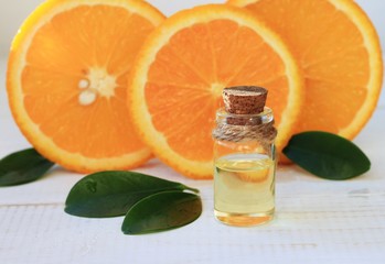 Essential orange oil in bottle, fresh fruit slices on background. Natural fragrances.