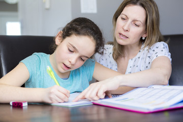 Mature mother helping her child with homework at home.