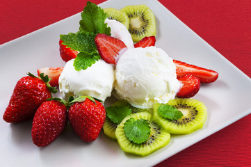 Butter and strawberry ice cream balls on the plate. Strawberries, kiwi, lemon balm