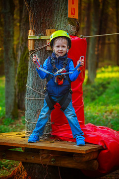 Portrait of happy little boy having fun in adventure park smiling to camera wearing helmet and safety equipment.