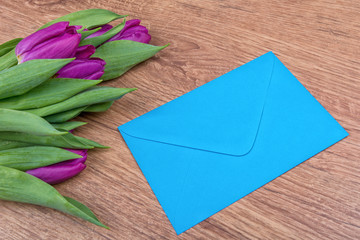 Blue envelope and violet tulips on a wooden background