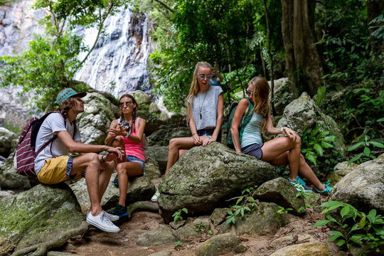 Young tourists are resting on the rocks in the jungle waterfall in the background
