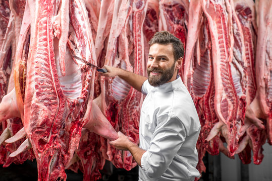 Handsome butcher cutting pork carcasse at the meat manufacturing
