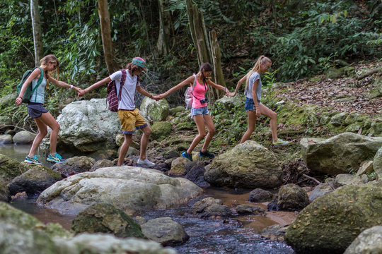 Young tourists are moving across the creek on the rocks in the jungle 

