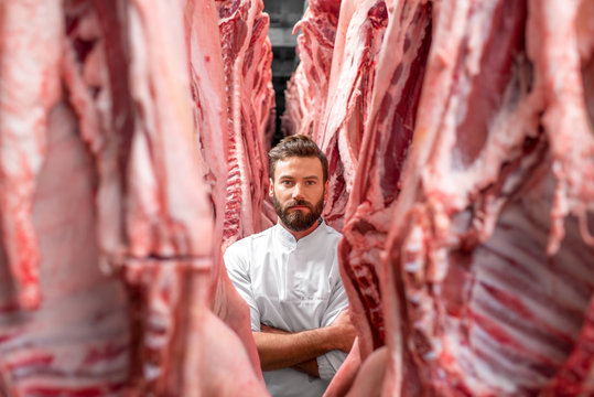 Portrait of a handsome butcher in white uniform with pork carcasses at the meat manufacturing 