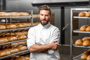 Tuinposter Portrait of handsome baker at the bakery with breads and oven on the background © rh2010