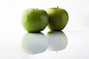 Two green fresh ripe apples on white background with reflection from side
