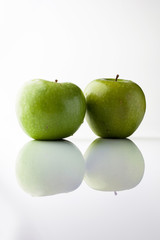 Two green fresh ripe apples on white background with reflection from side vertical composition