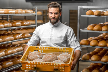 Handsome baker holding box full of freshly baked buckweat breads at the manufacturing - obrazy, fototapety, plakaty