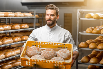 Handsome baker holding box full of freshly baked buckweat breads at the manufacturing