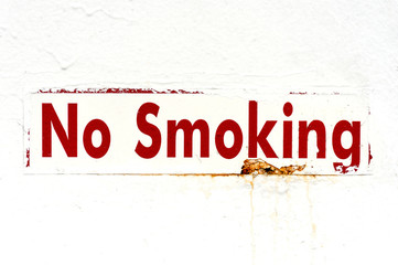 Rusty metal sign with red letters on white ground: No Smoking