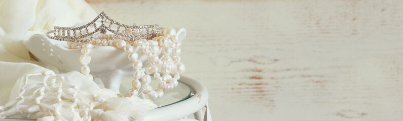 website banner background of white pearls necklace and diamond tiara on vintage table. toned image....