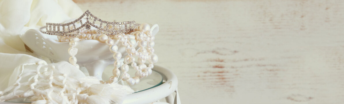 website banner background of white pearls necklace and diamond tiara on vintage table. toned image. selective focus
