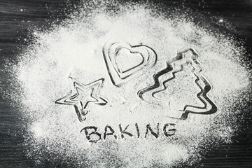 Cookie cutters shaped with flour lying on black background. Baking cookies concept. Word backing.