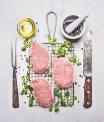 Fresh raw pork steaks with herbs, a knife and fork for the meat on the grill for roasting on wooden...