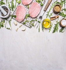 pork steaks on the grill for roasting with meat fork, butter, rosemary and arugula border ,place for text  on wooden rustic background top view