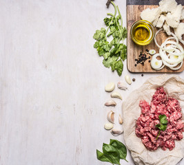 Ingredients for cooking homemade mincemeat on paper, parsley, garlic, onion bun and oils, border ,place for text  on wooden rustic background top view
