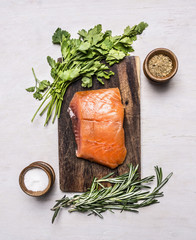 piece of smoked salmon on a cutting board with herbs and spices on wooden rustic background top view
