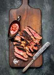 Sliced grilled Beef steak with knife and fork for meat on wooden cutting board
