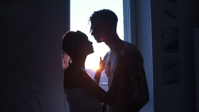Man and woman are kissing on sunset near the window after shower