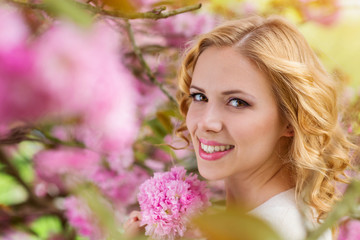 Fototapeta premium Blond woman, curly hair against pink tree in blossoom