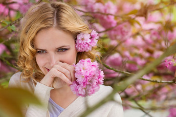 Fototapeta premium Blond woman, curly hair against pink tree in blossoom