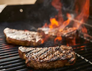 Crédence de cuisine en verre imprimé Grill / Barbecue Biftecks de contre-filet de New York avec os cuits sur un gril flamboyant