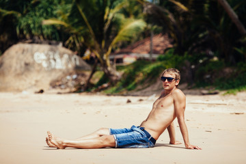 Man relaxing on a tropical beach. Young tanned man taking sunbat