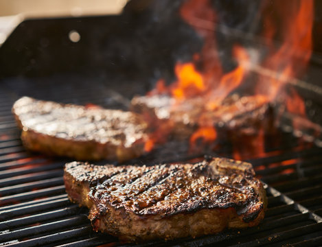 Bone-in New York Strip Steaks Cooking Over Flaming Grill