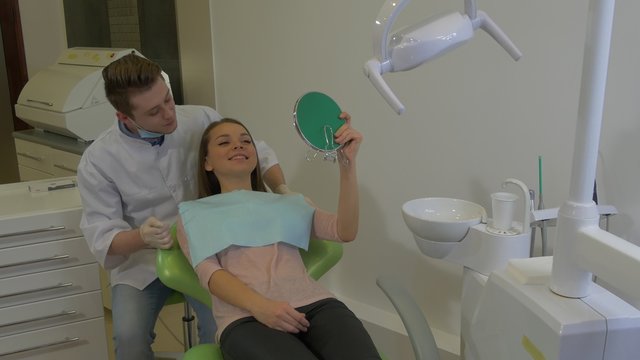 Patient is Looking at Mirror Dentist is Talking Takes a Mirror Young Male Doctor and Female Client of a Dental Clinic in a Chair Visit to a Stomatologist