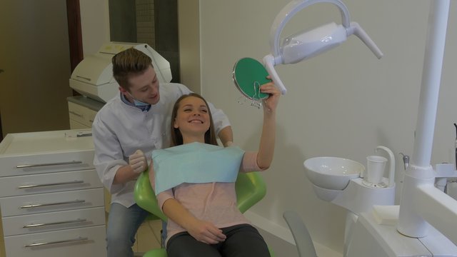 Woman is Looking at Mirror Dentist is Talking Young Male Doctor and Female Client of a Dental Clinic in a Chair Happy Client Visit to a Stomatologist