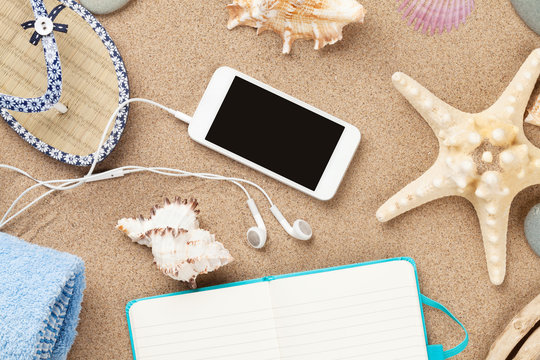 Smartphone and notepad on sea sand with starfish and shells