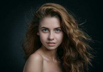 Dramatic portrait of a girl theme: portrait of a beautiful girl with flying hair in the wind against a background in studio