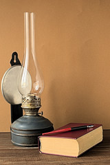 Old kerosene lamp.   Old kerosene lamp and a book on a brown background
 