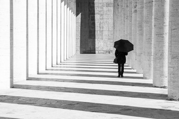 Donna con ombrello in un corridoio porticato in bianco e nero 