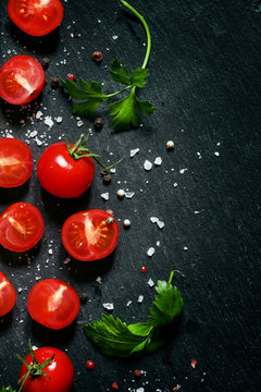 Cut cherry tomatoes on a black background with spices, top view