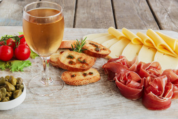 delicious appetizer to wine - ham,prosciutto, cheese, capers, tomato, served on a light wooden board