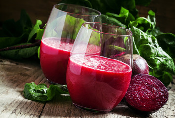 Beetroot smoothie in a large glass, fresh beets with tops, old w