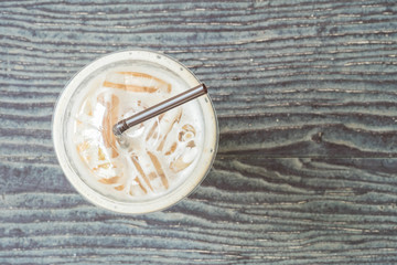 Closeup top view of plastic cup of coffee on blurred wooden table textured background