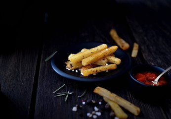 French fries on a black saucer, red sauce on a dark background
