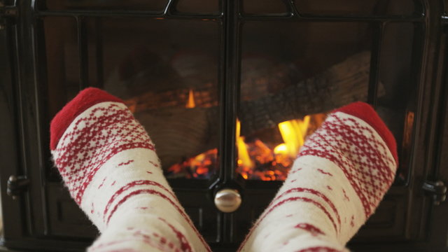 Feet in socks warming by fire in fireplace. Girl is wearing socks nearby fireplace. Female is relaxing at home during winter. SLOW MOTION.