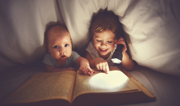 children brother and sister read a book with aflashlight under b
