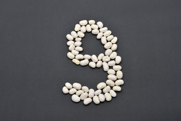 Fototapeta na wymiar Number nine made from white beans on black background. Food vega