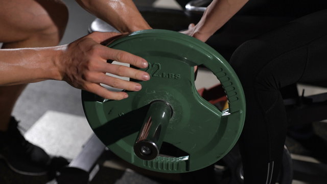 bodybuilder puts weight on the barbell. Communicates with a pretty athlete
