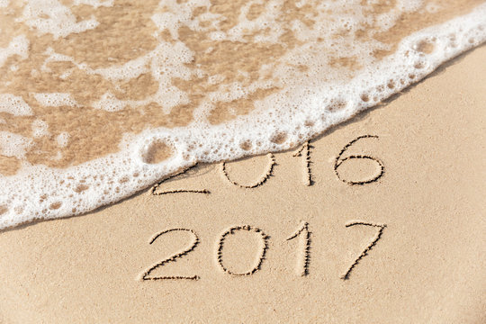 2016 2017 inscription written on wet yellow beach sand being washed by sea wave